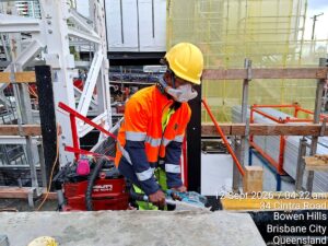 Worker in hi-vis sanding concrete with an extraction sander while wearing an AYO WX half-face powered respirator, Brisbane