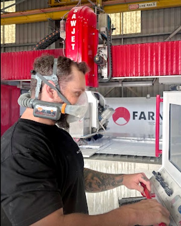 Platinum Stone Co stonemason operating a CNC stone saw while wearing an AYO WX powered air-purifying respirator
